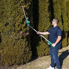 model using the trimmer on tall hedges 
